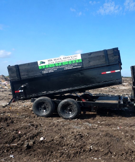 Mr. Haul Away branded dump trailer tipped at the disposal site under a blue Florida sky